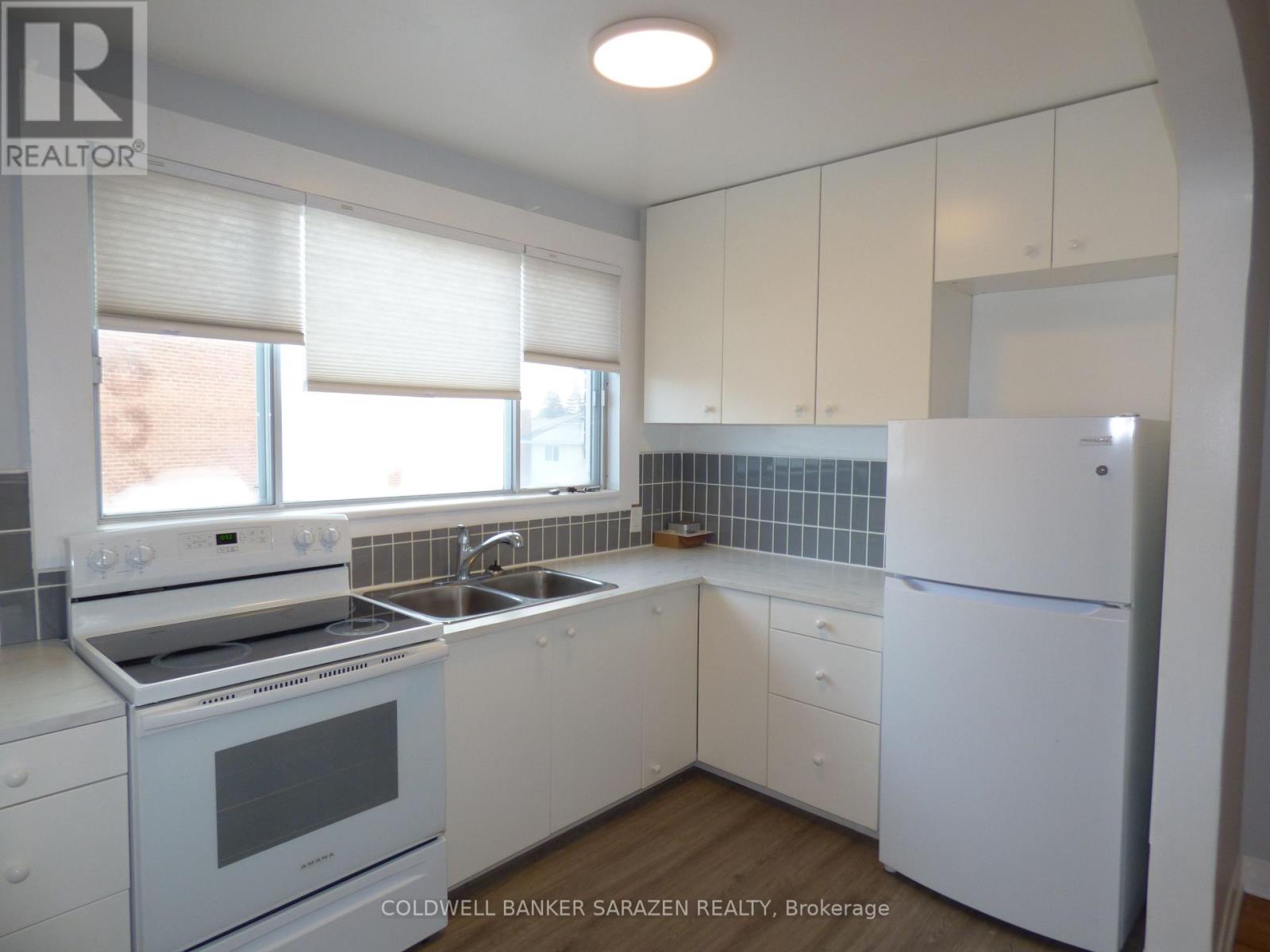 A white kitchen with a refrigerator, stove, and sink.