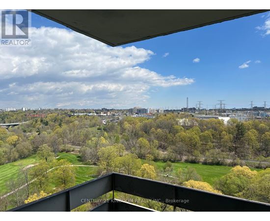 A view from a balcony overlooking a green landscape with trees and buildings in the distance.