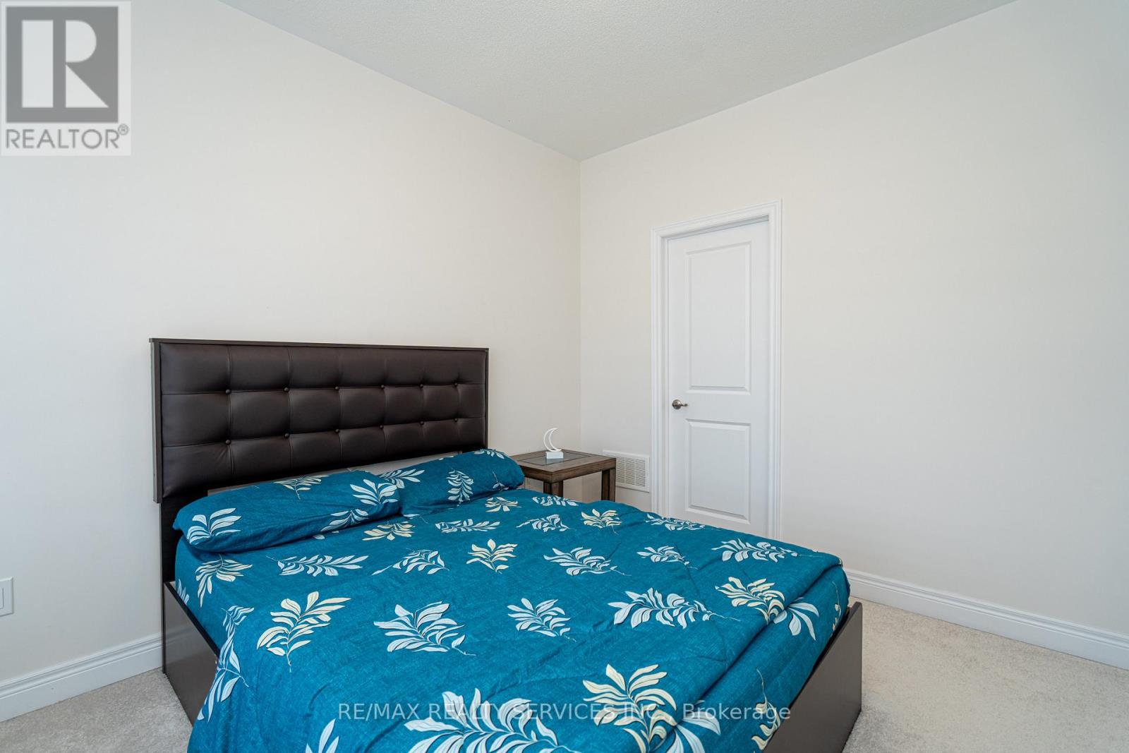 A bedroom with a bed covered in a blue leaf patterned sheet.