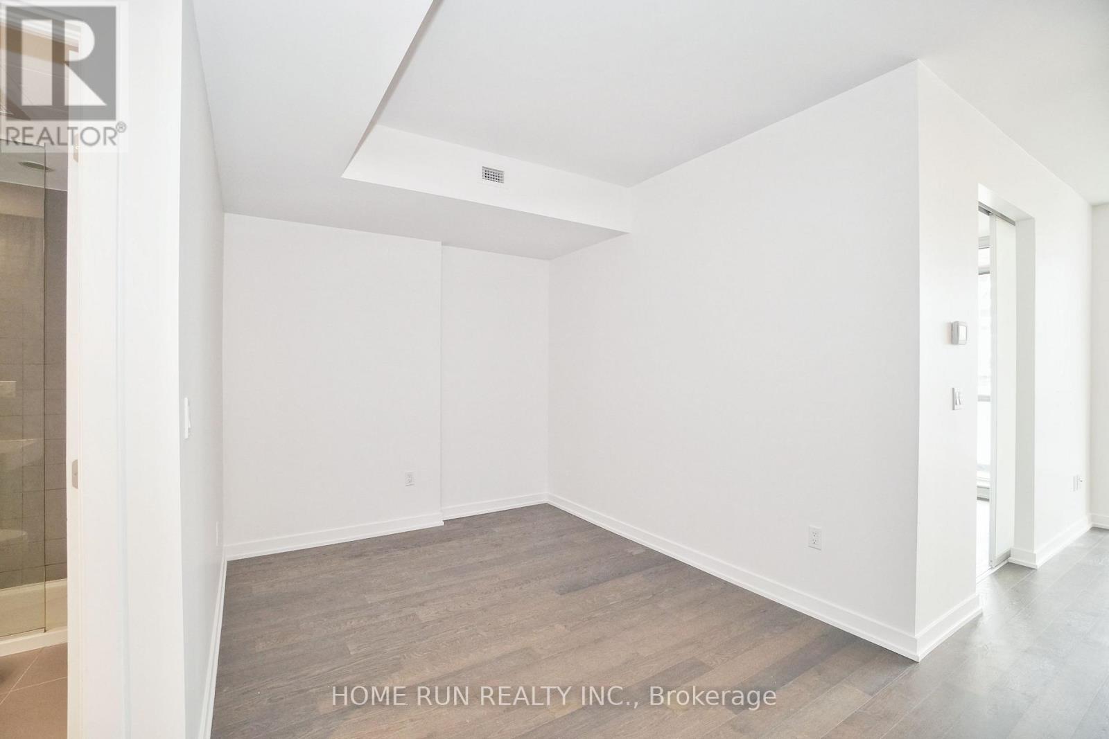 A spacious empty room with white walls and wooden flooring.