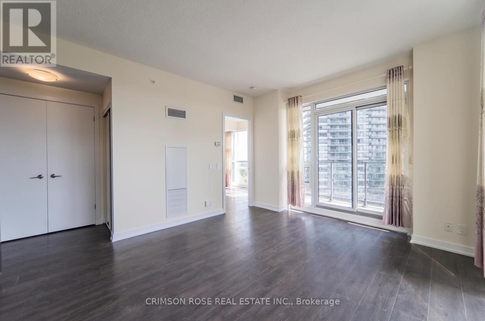 A spacious room with hardwood floors and a large window with curtains.