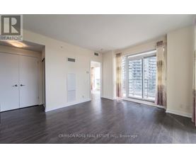 A spacious room with hardwood floors and a large window with curtains.