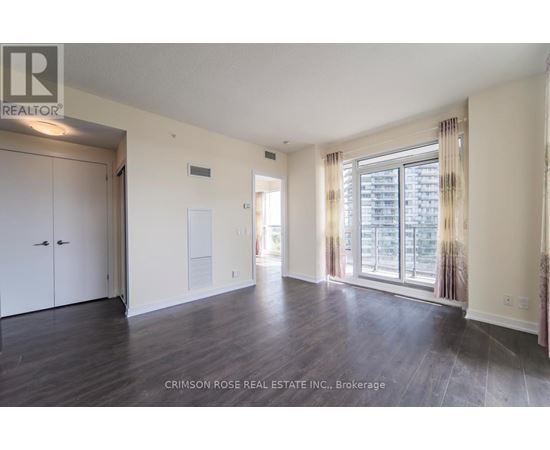 A spacious room with hardwood floors and a large window with curtains.