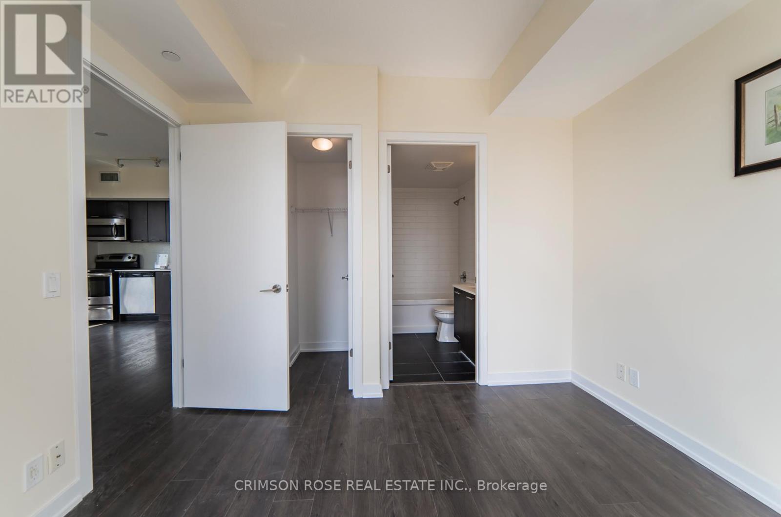 A real estate listing photo of a white bedroom with a white door and a white toilet.