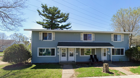 A two-story house with a front porch and a tree in the front yard.