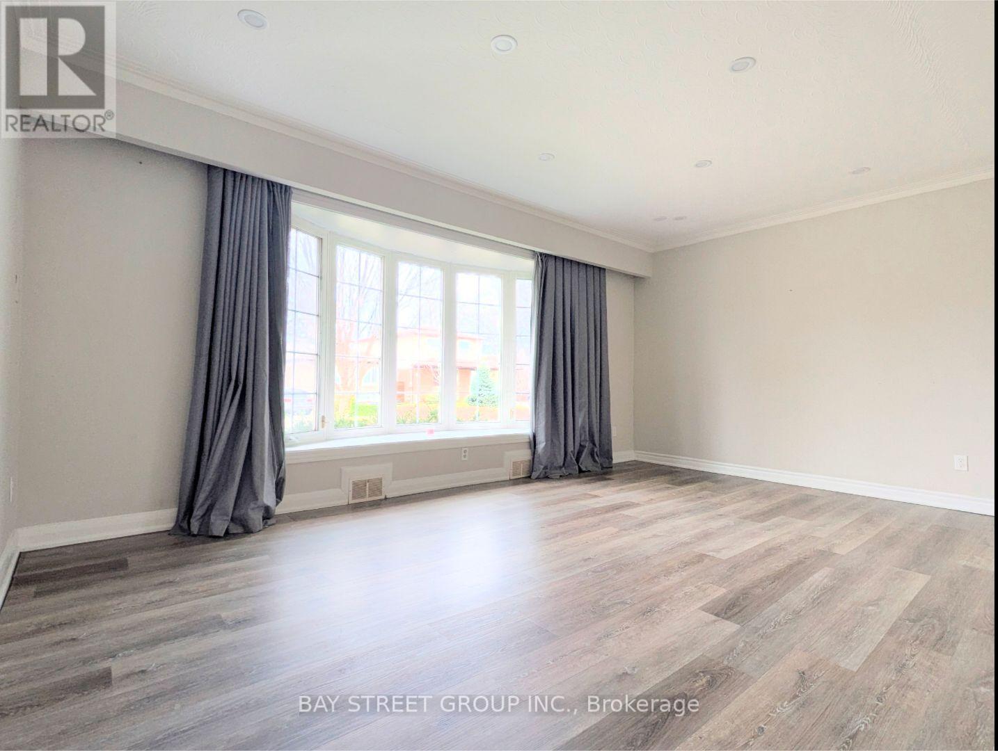 A spacious room with wooden flooring and grey curtains.