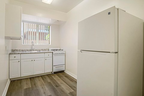 A white refrigerator stands in a kitchen with wooden floors and white cabinets.