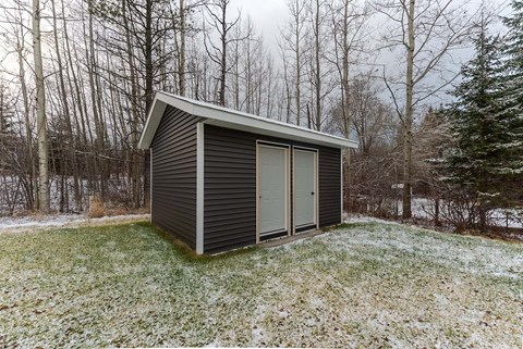 A small house with a grey roof and a grey wall is surrounded by trees.