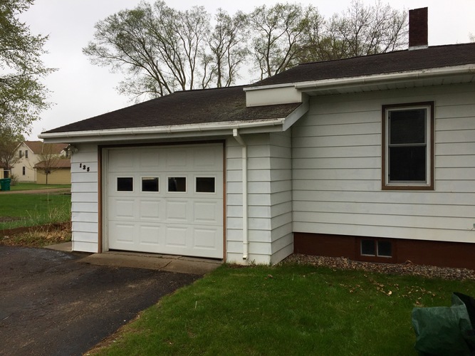 A white house with a brown roof and a white garage door.