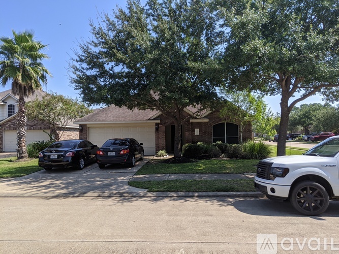Two cars are parked in front of a house with a tree and a palm tree in the background.
