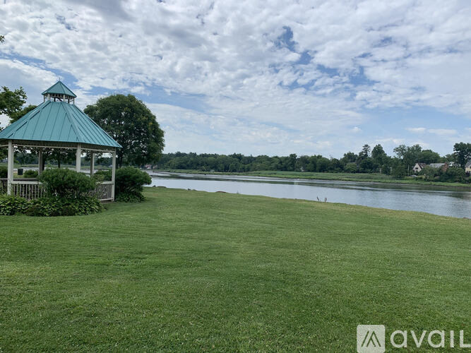 A gazebo sits on a grassy field next to a body of water.