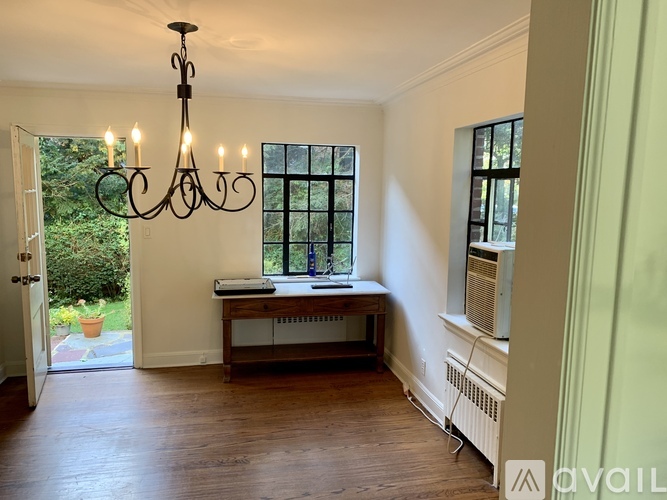 A room with a chandelier, a window with a view of trees, and a wooden bench with a console table.