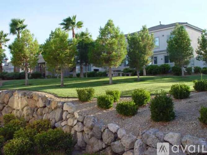 A stone wall borders a well-manicured lawn in front of a house.