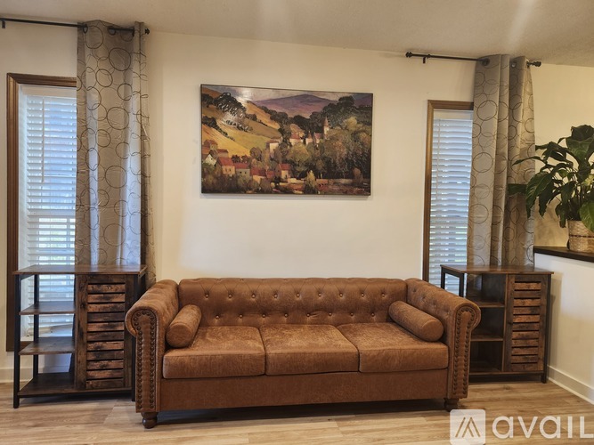 A brown couch sits in a living room with a painting on the wall.