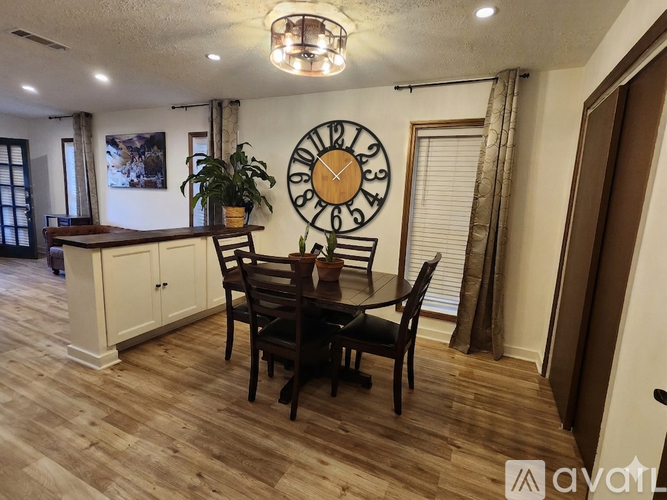 A dining room with a wooden table and chairs, a clock on the wall, and a potted plant on the counter.