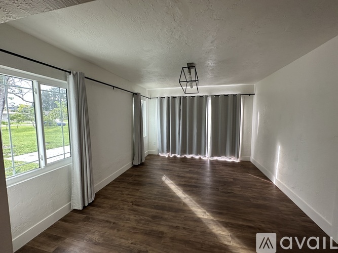A room with wooden floors and white walls, with a hanging light fixture and a window with curtains.
