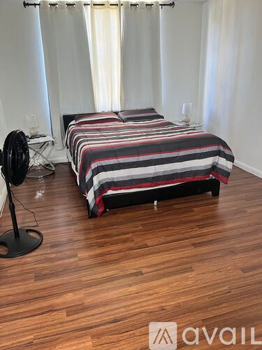A bedroom with a striped bed and a fan on the floor.