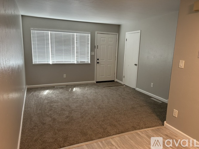 A room with a carpeted floor, two doors, and a window with blinds.