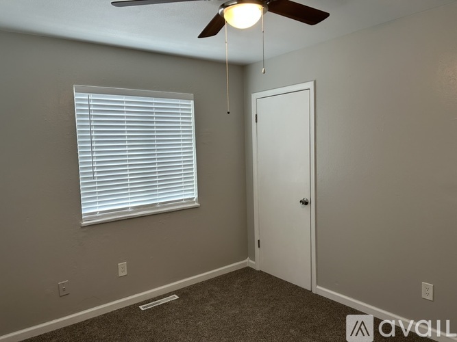 A room with a ceiling fan, a window with blinds, and a door.