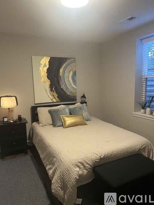 A bedroom with a large bed, a nightstand with a lamp, and a painting on the wall.