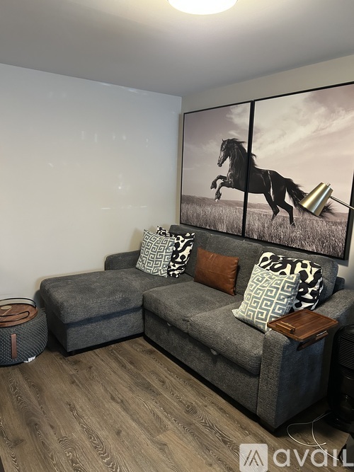 A living room with a grey couch and a painting of a horse on the wall.