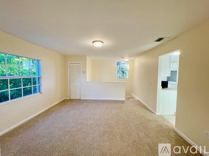 A room with carpeted floor, a window with a view of trees and a white door.