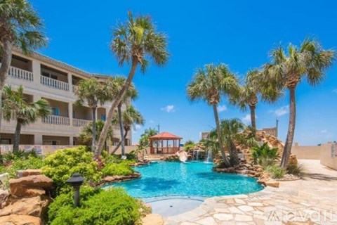 A pool surrounded by palm trees and a building in the background.