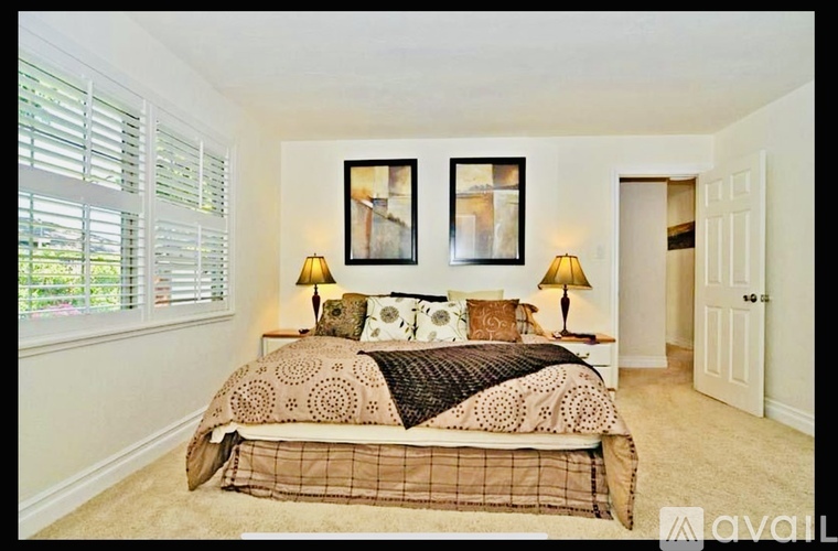 A bedroom with a bed, two lamps, and two pictures on the wall.