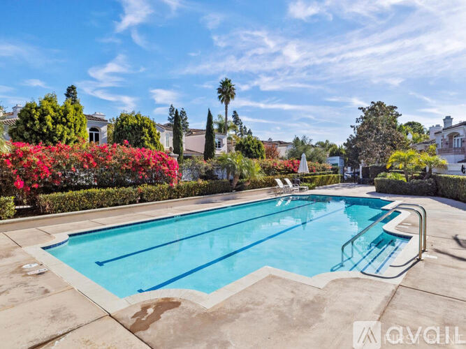 A swimming pool surrounded by a garden with red flowers and trees.