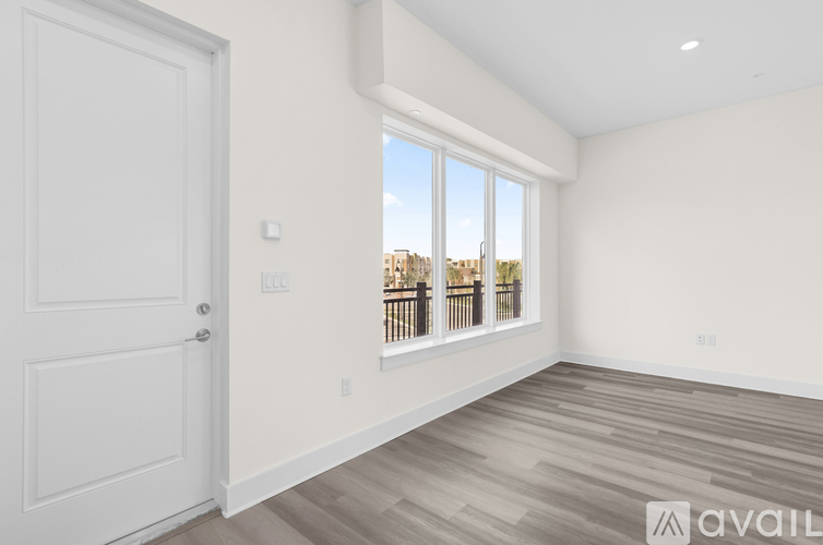 A room with a white door and a window with a view of a balcony.