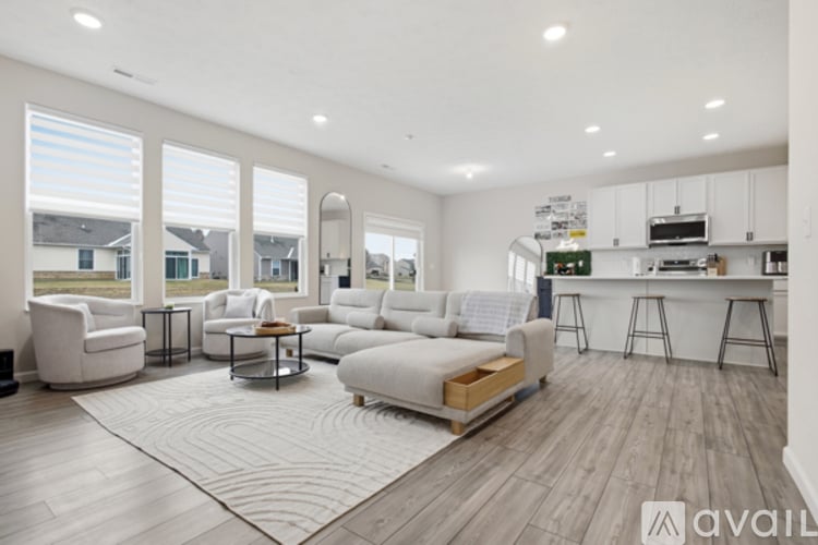 A spacious living room with white furniture and a kitchen area in the background.