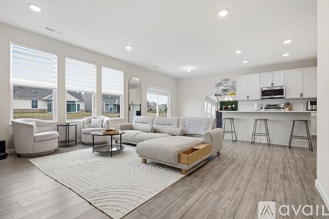 A spacious living room with white furniture and a kitchen area in the background.