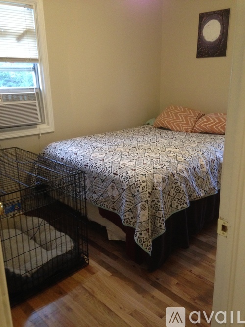 A bedroom with a bed, a dog crate, and a picture on the wall.