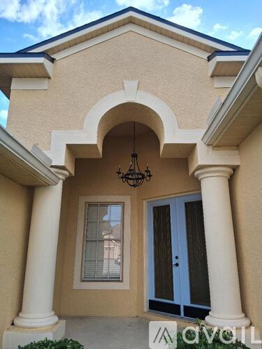 A beige house with a blue door and a chandelier hanging from the arch.