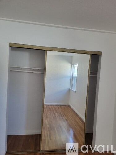 A large mirror with a wooden frame is leaning against a wall in a room with wooden flooring.