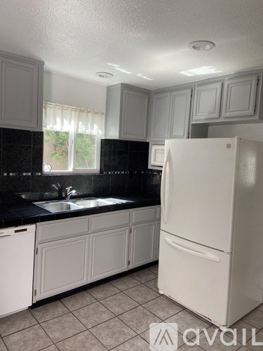 A white refrigerator in a kitchen with black countertops.