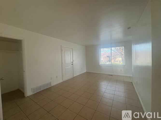 A spacious room with tiled flooring and white walls, with a window showing a view of a building outside.