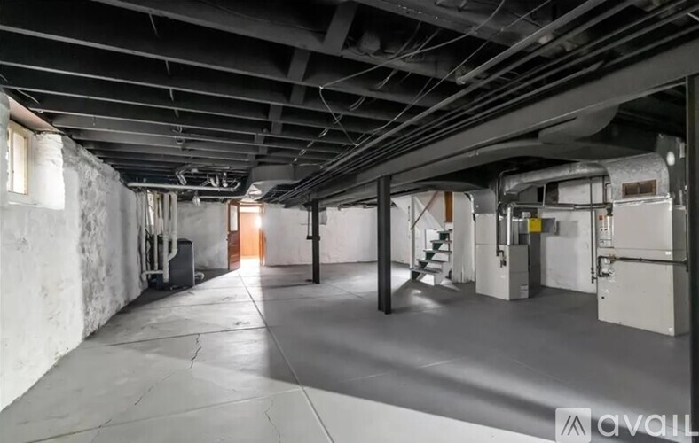 A spacious industrial-style room with a concrete floor and exposed ceiling pipes.
