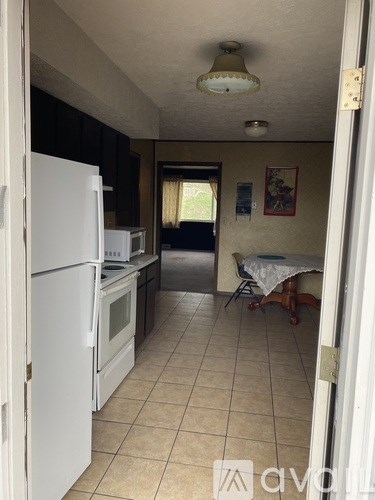 A kitchen with white appliances and a table with chairs in the background.