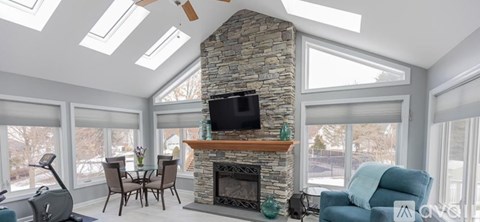A living room with a stone fireplace and a television mounted above it.