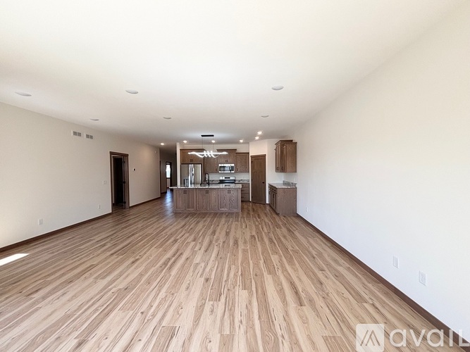 A spacious room with wooden flooring and a kitchen area in the background.