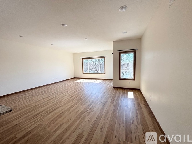 A spacious room with wooden flooring and two windows.