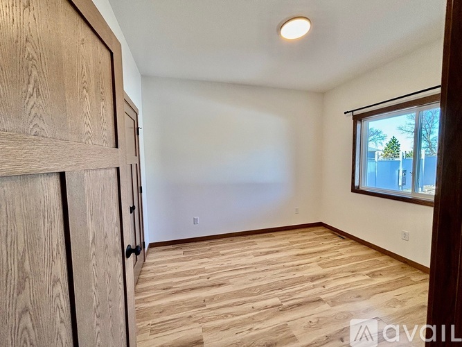 A room with wooden flooring and a window showing a view of trees and a fence.