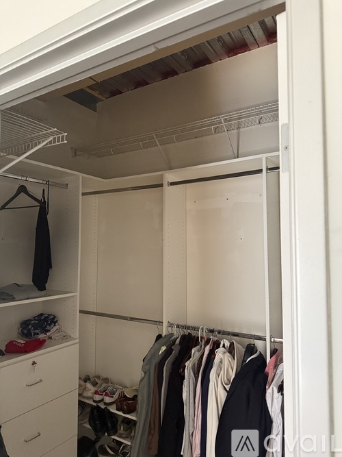 A white closet with clothes hanging and shoes on the floor.