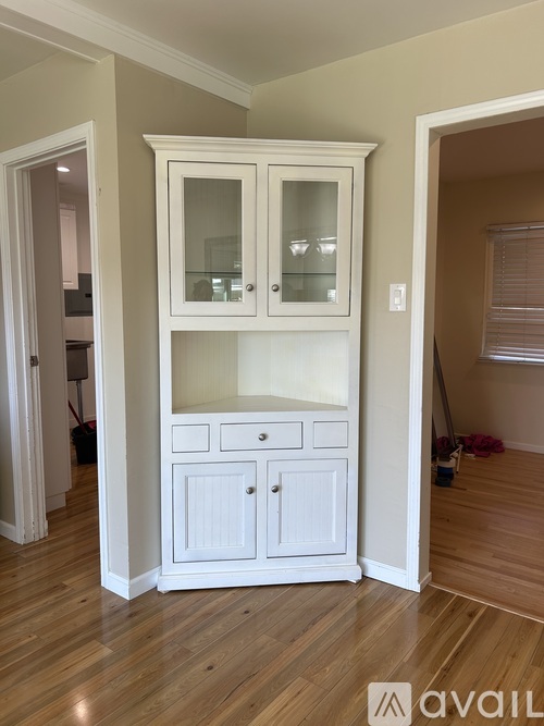A white cabinet with glass doors and drawers is in a room with wooden floors.