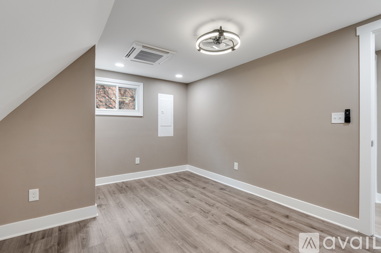 A room with beige walls and wooden flooring, with a window showing trees outside.
