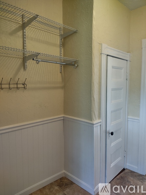 A white door is in a room with a white wall and a shelf above it.