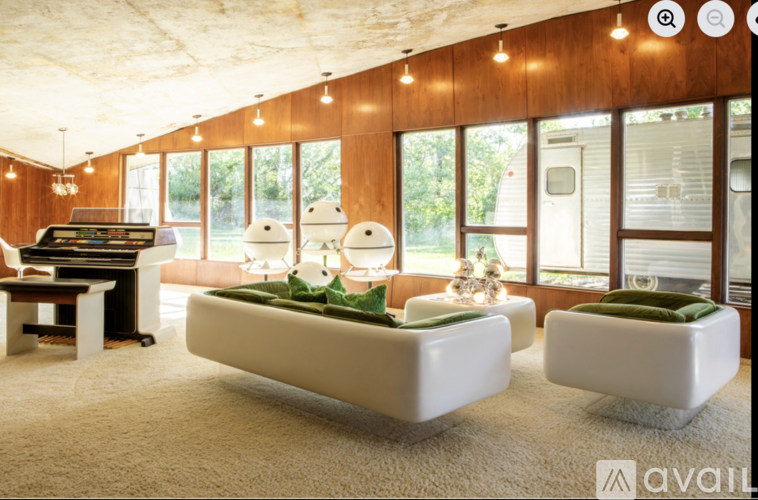 A living room with a piano and two white ottomans.