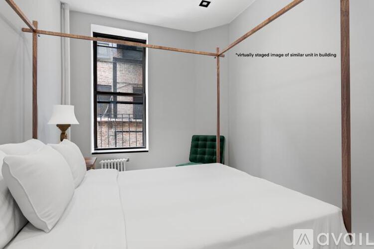 A bedroom with a white bed and a window with a view of a building outside.