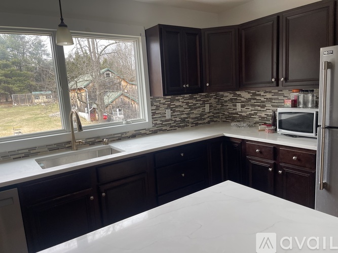 A kitchen with a white countertop and a window overlooking a backyard.